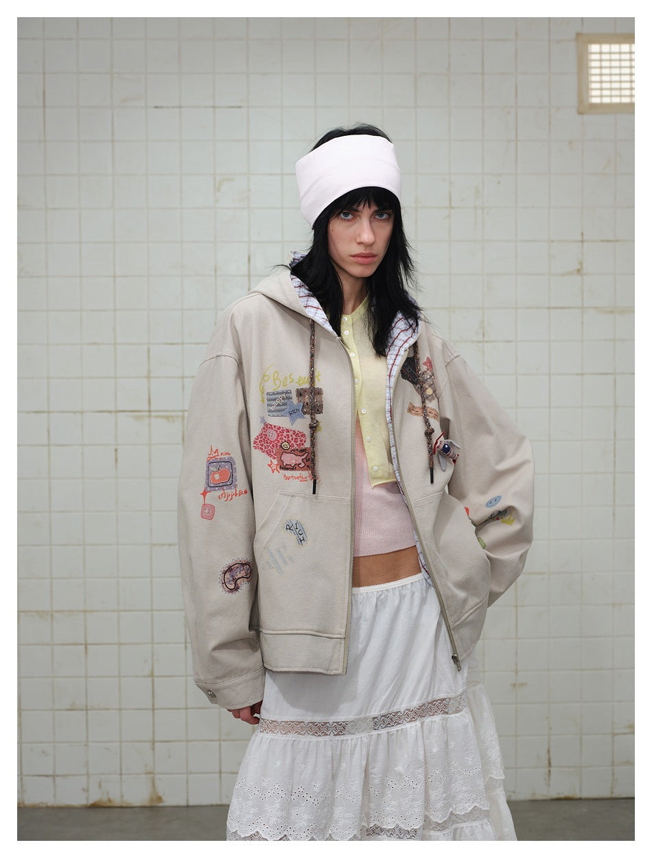 Model wearing an open taupe hoodie with colorful patches over a pale yellow top and a white lace-trimmed skirt.