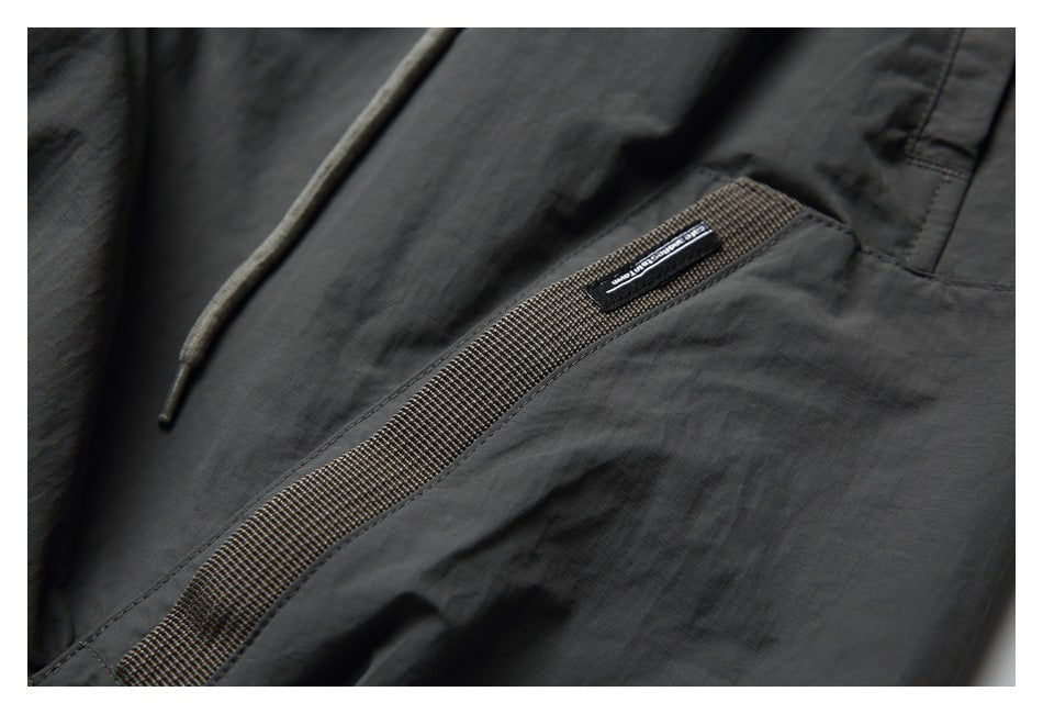 Close-up of charcoal pants with a drawcord, woven pocket trim, and a small sewn label.