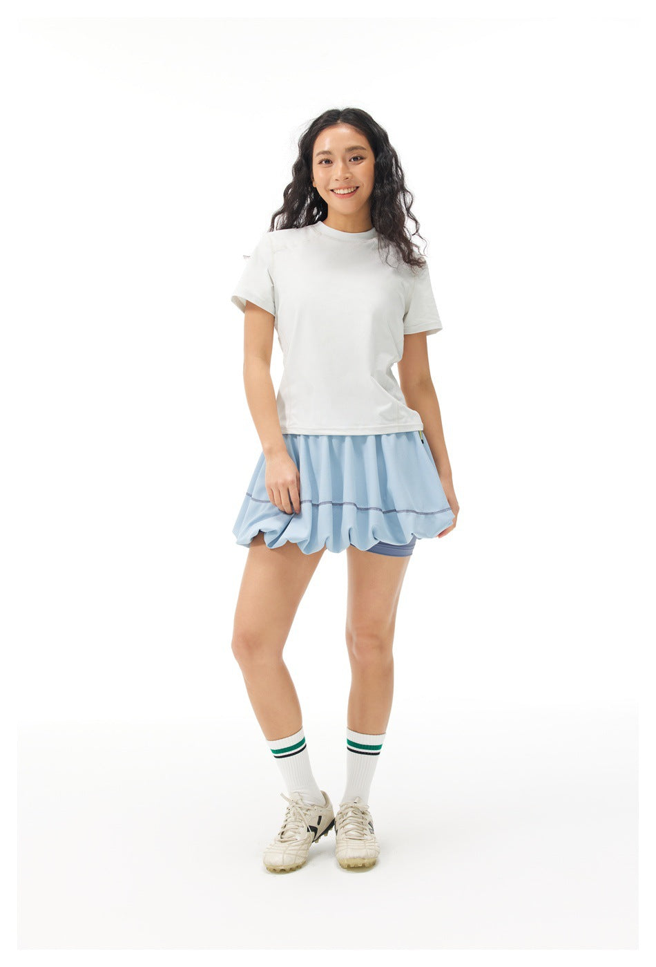 Full-length front view of a model in a white short-sleeve top, light blue bubble skirt, striped socks and sneakers.