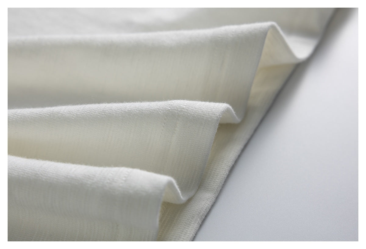 White knit fabric folded into layered ridges, showing its fine texture and edge.