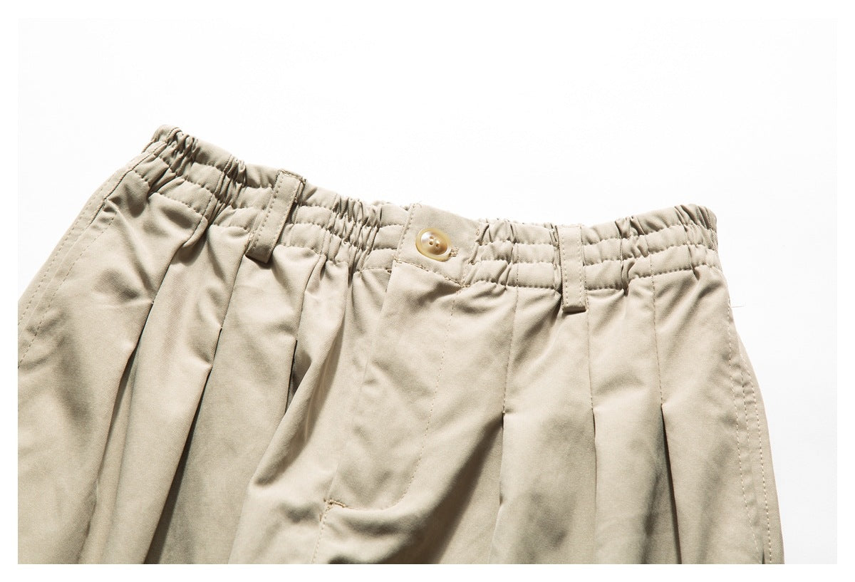 Close-up of light beige pants showing the gathered elastic waistband, button, belt loops, and front pleats.