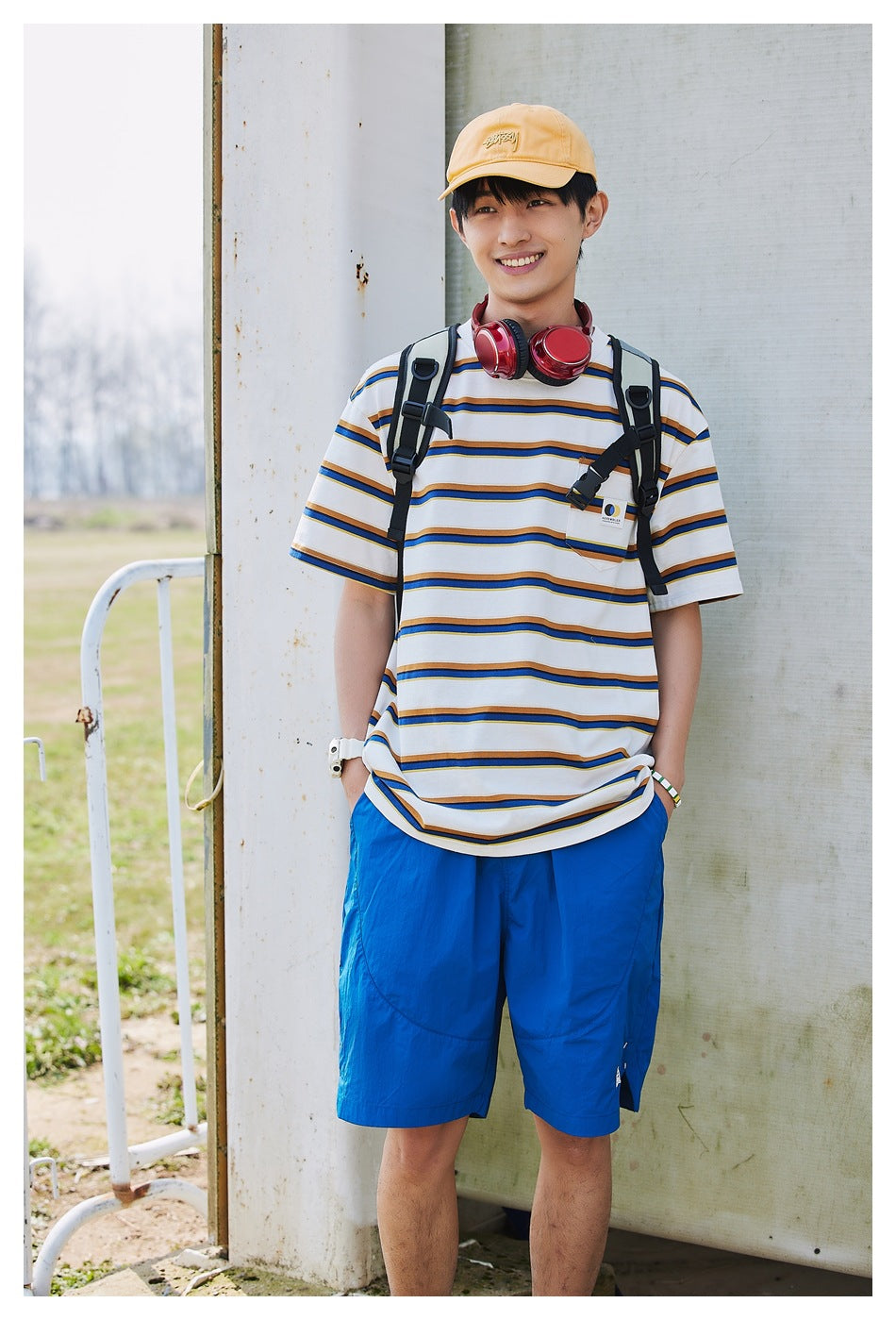 Front view of a smiling model in a white T-shirt with navy and mustard stripes and bright blue shorts.