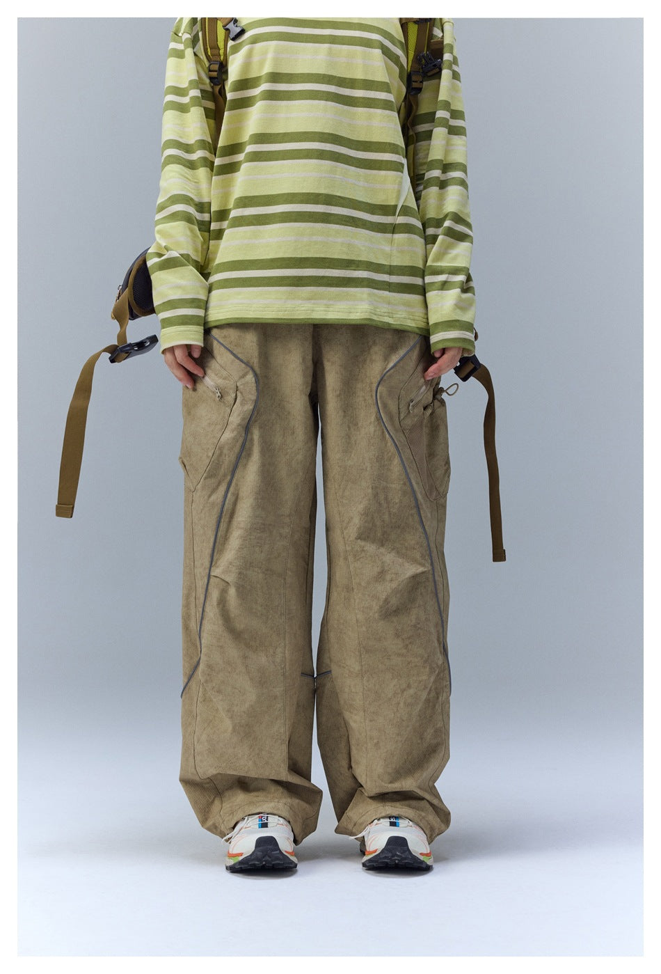 Front view of a model wearing loose khaki cargo pants with curved piping and large side pockets.