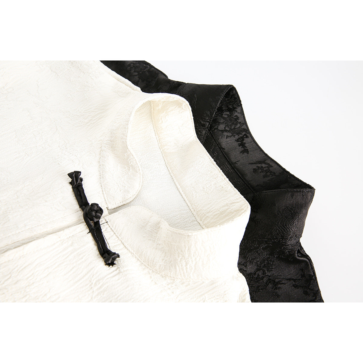 Close-up of an ivory mandarin-collar jacket with a black knotted frog closure and black floral-patterned fabric behind it.