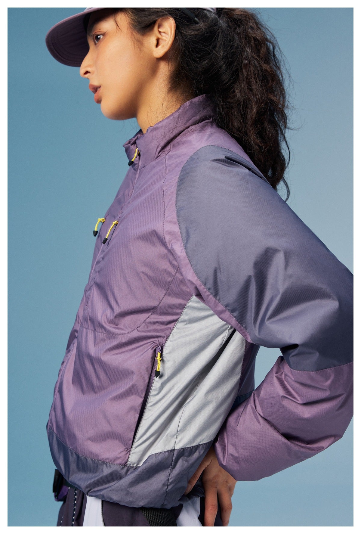 Close-up of the jacket’s lavender body, charcoal sleeve, pale side panel, and yellow pocket zipper pull.