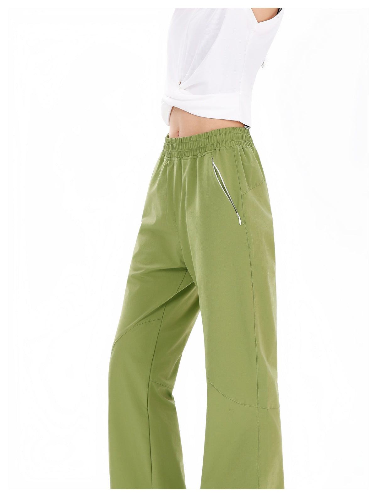 Close view of olive-green pants showing the gathered waistband, side pocket, and white zipper detail on a model.