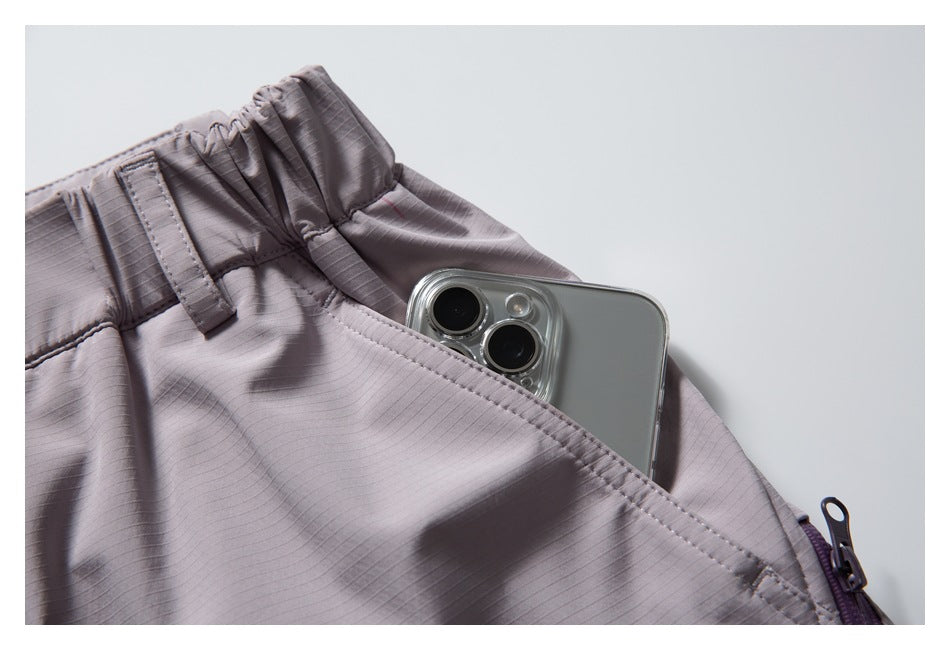 Close-up of mauve-gray pants with a phone partly tucked into a slanted pocket below the elastic waistband.