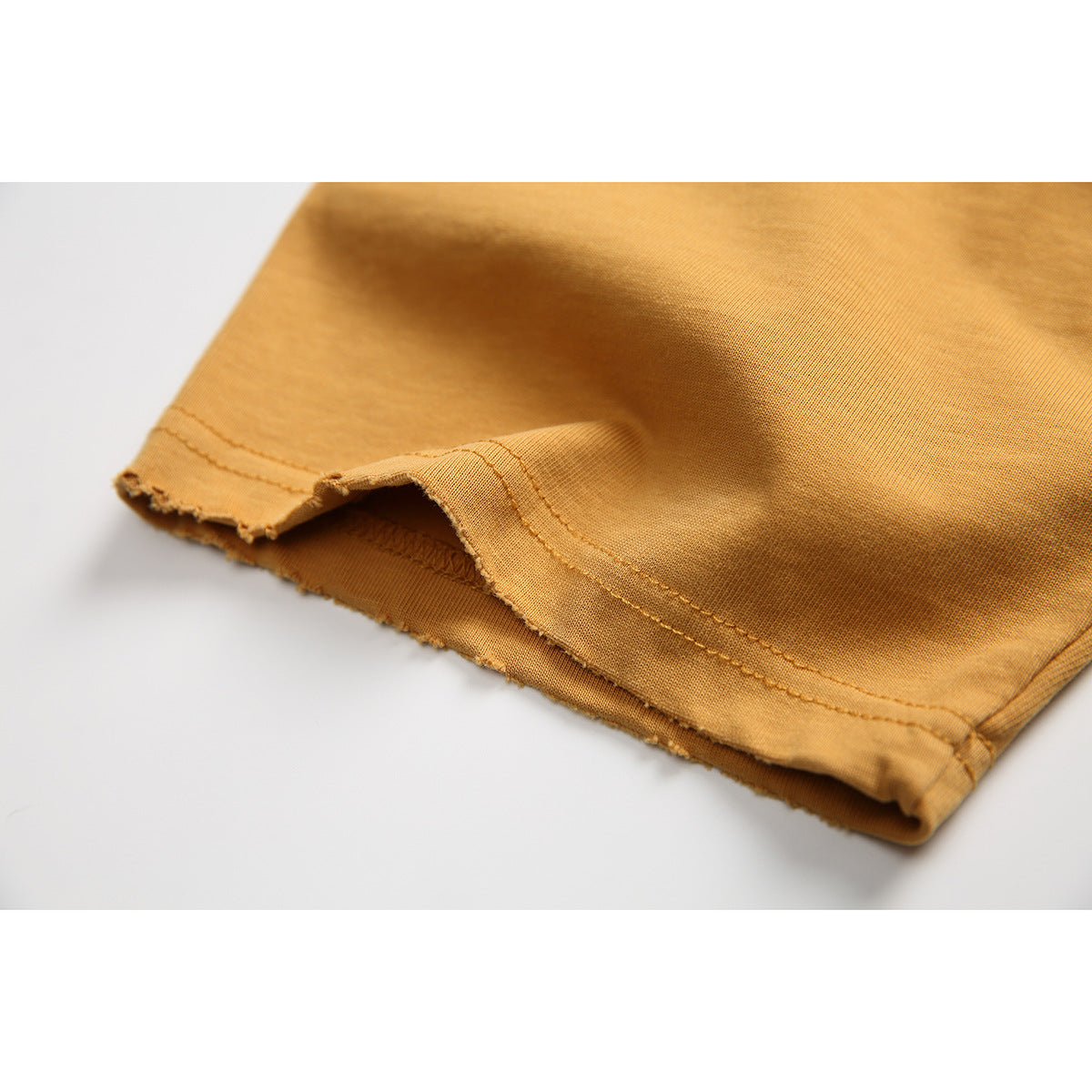 Close-up of a mustard-gold T-shirt hem showing double stitching and the fabric edge.