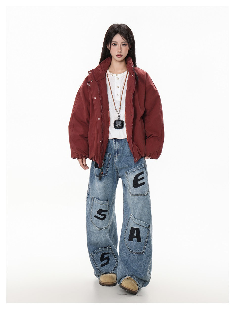 Front view of a model in a burgundy oversized jacket and loose blue jeans with black lettering.