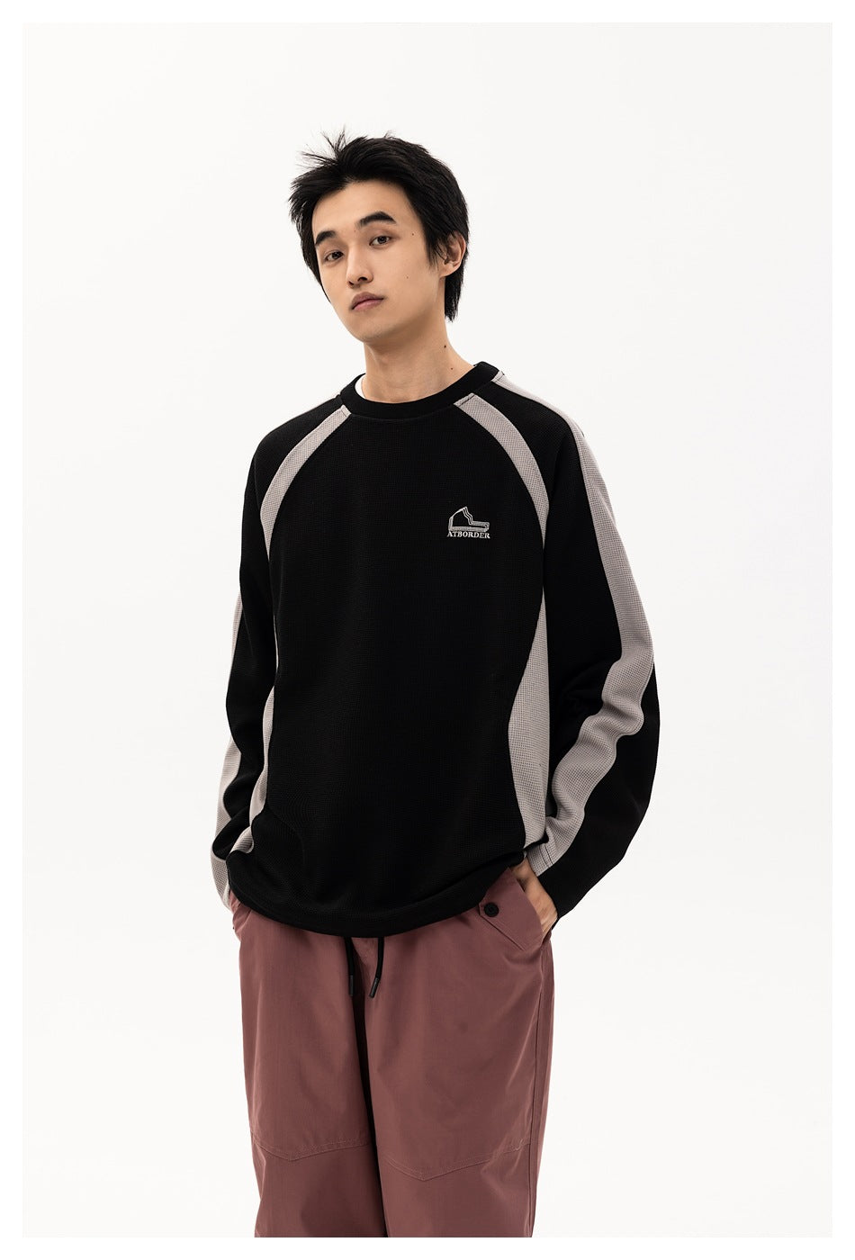 Model shown from the front wearing a black sweatshirt with gray raglan panels and dusty mauve pants.