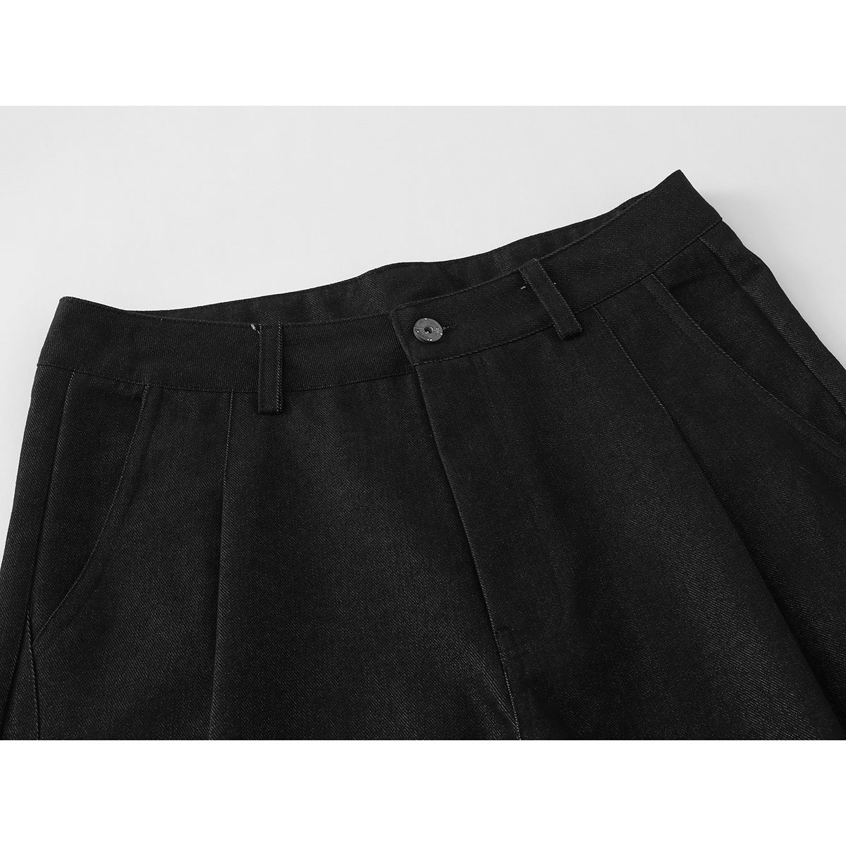 Close-up of black shorts showing the waistband, button closure, belt loops, and front pleats.