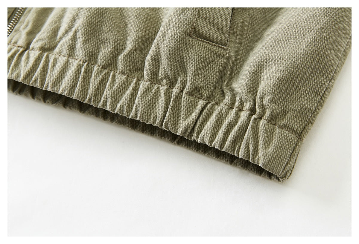 Close-up of the gathered elastic hem and lower pocket area of an olive khaki jacket.