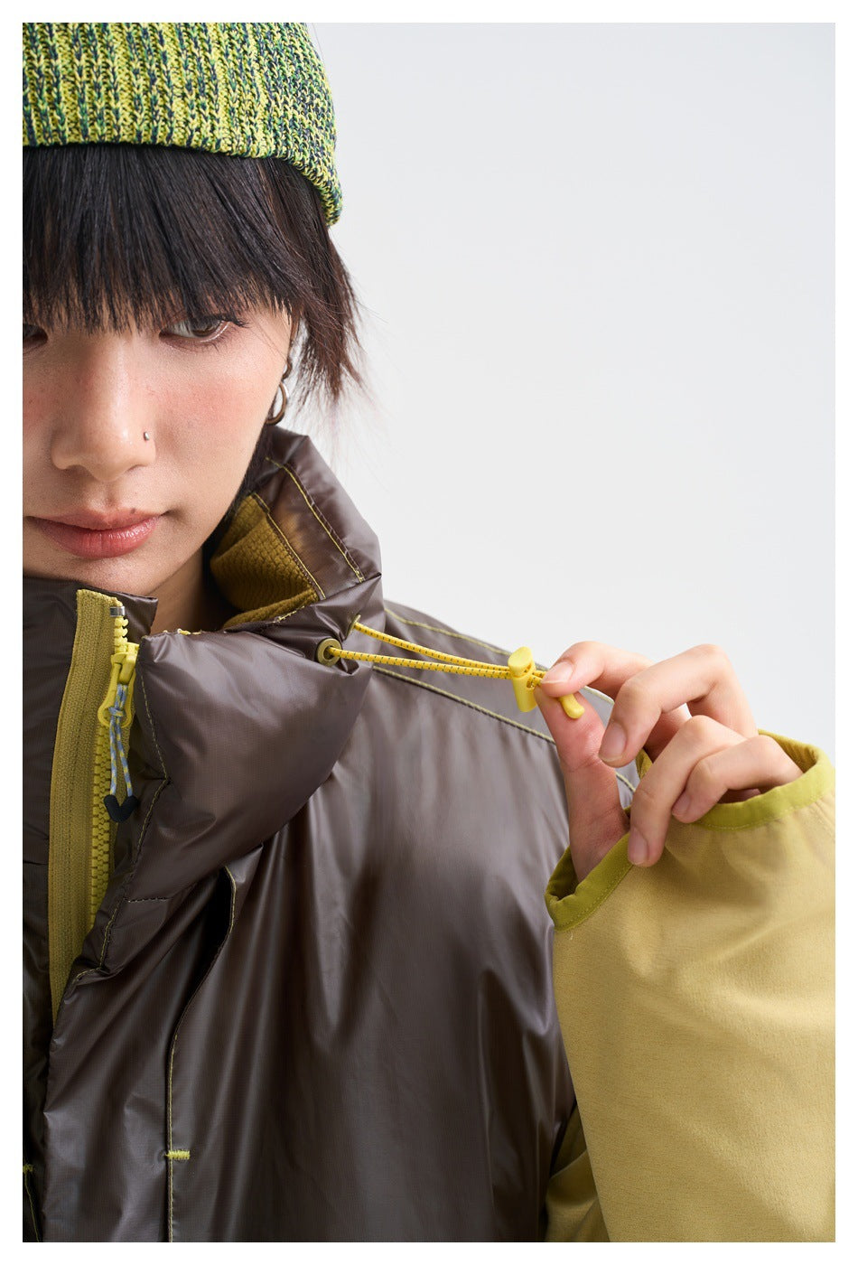 Close-up of a model wearing a dark brown vest, showing the yellow collar drawcord and zipper details.