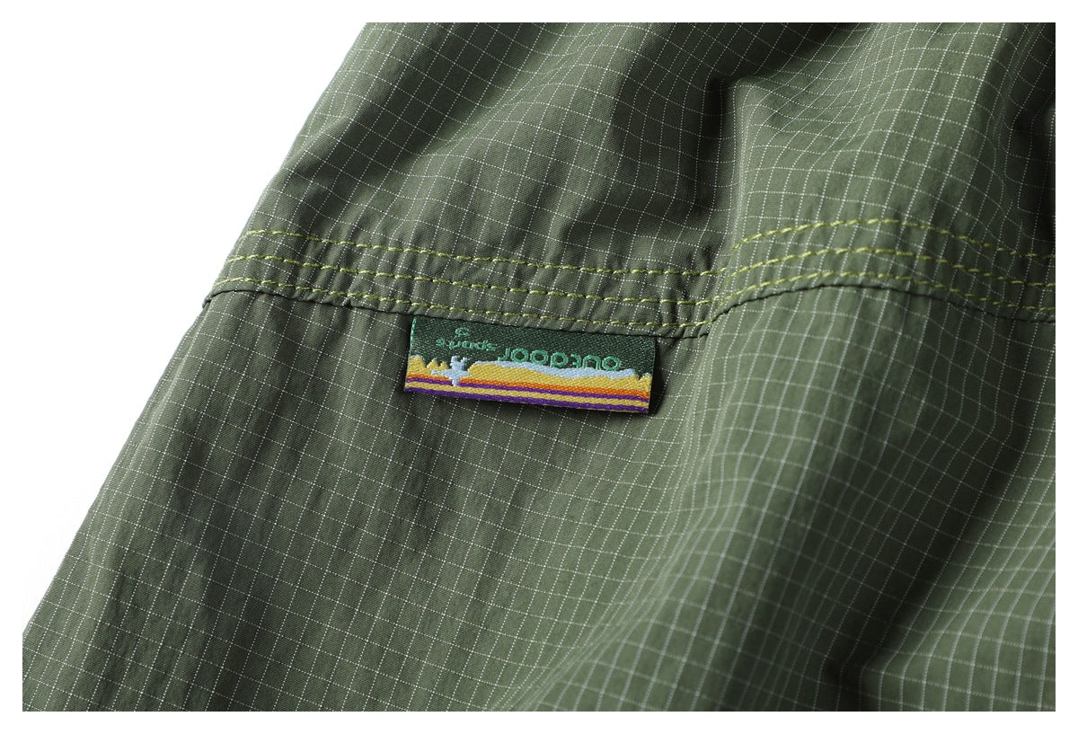 Close-up of an olive green grid-patterned garment showing a small sewn label beneath stitched seams.