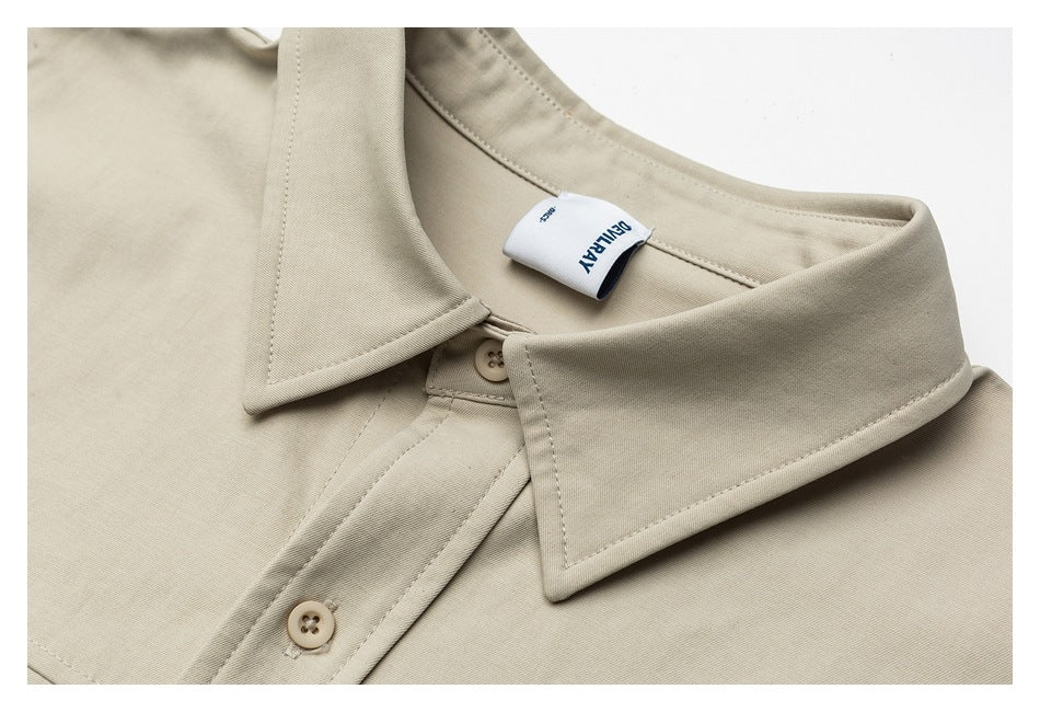 Close-up of a beige shirt collar, button placket, stitching, and sewn-in neck label.