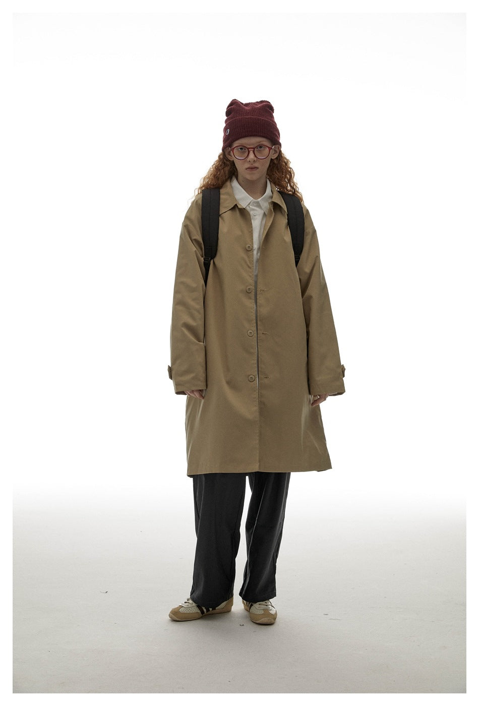 Front view of a model wearing a long tan button-front coat with a pointed collar and cuff tabs.