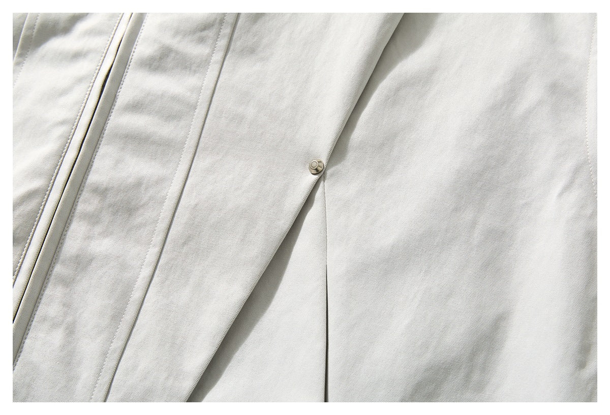 Close-up of an off-white jacket showing a small snap, stitched panels, and a seam.