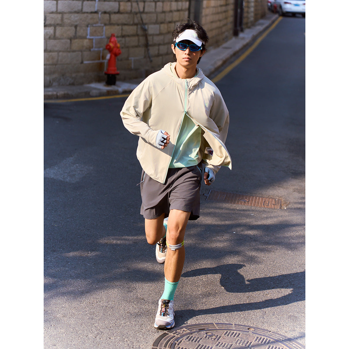 Man running outdoors in a light beige hooded zip jacket over a mint shirt and dark shorts.