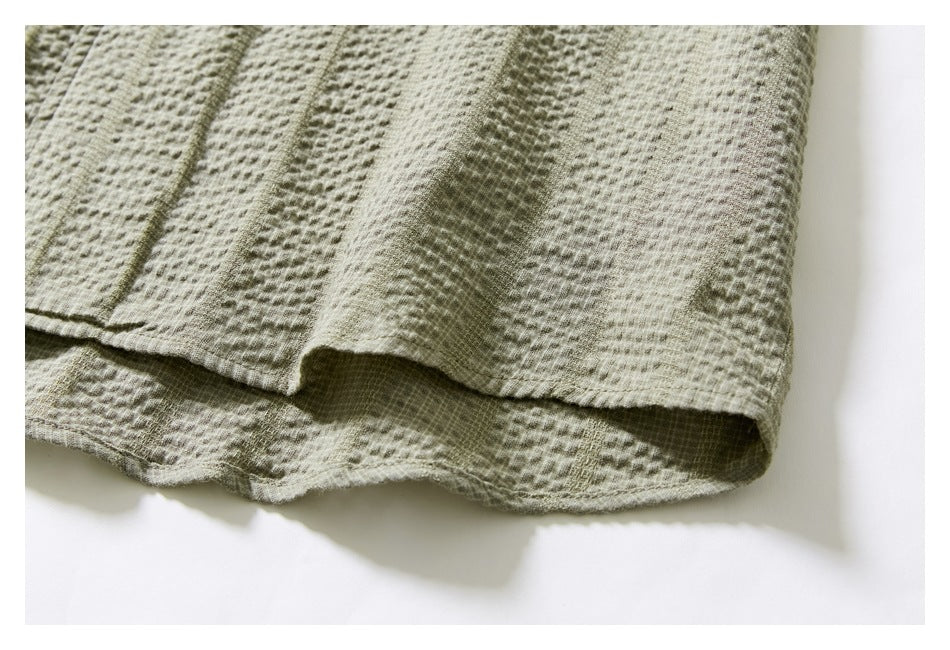 Close-up of the light olive shirt's textured fabric and layered hem edge.