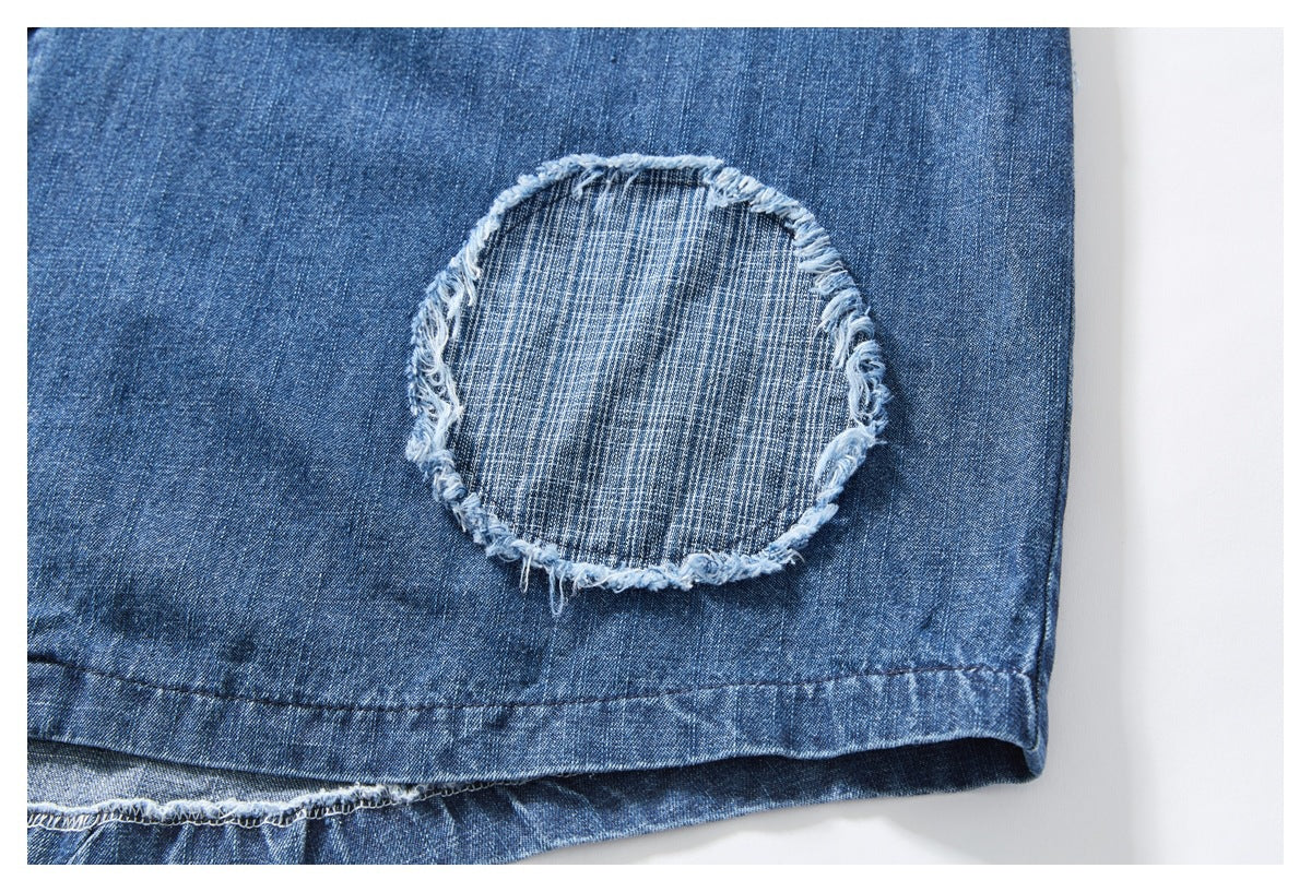 Close-up of a frayed circular patch on the blue denim shirt near the hem.