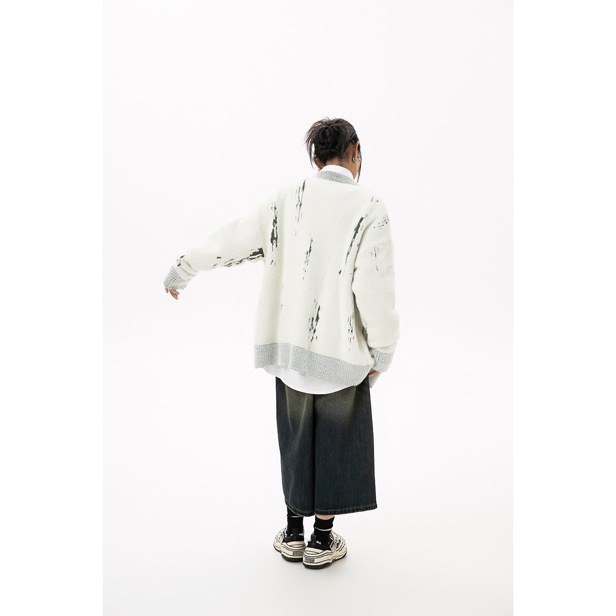 Back view of the ivory cardigan with gray hem and cuffs and sparse dark green abstract motifs, worn by a model.
