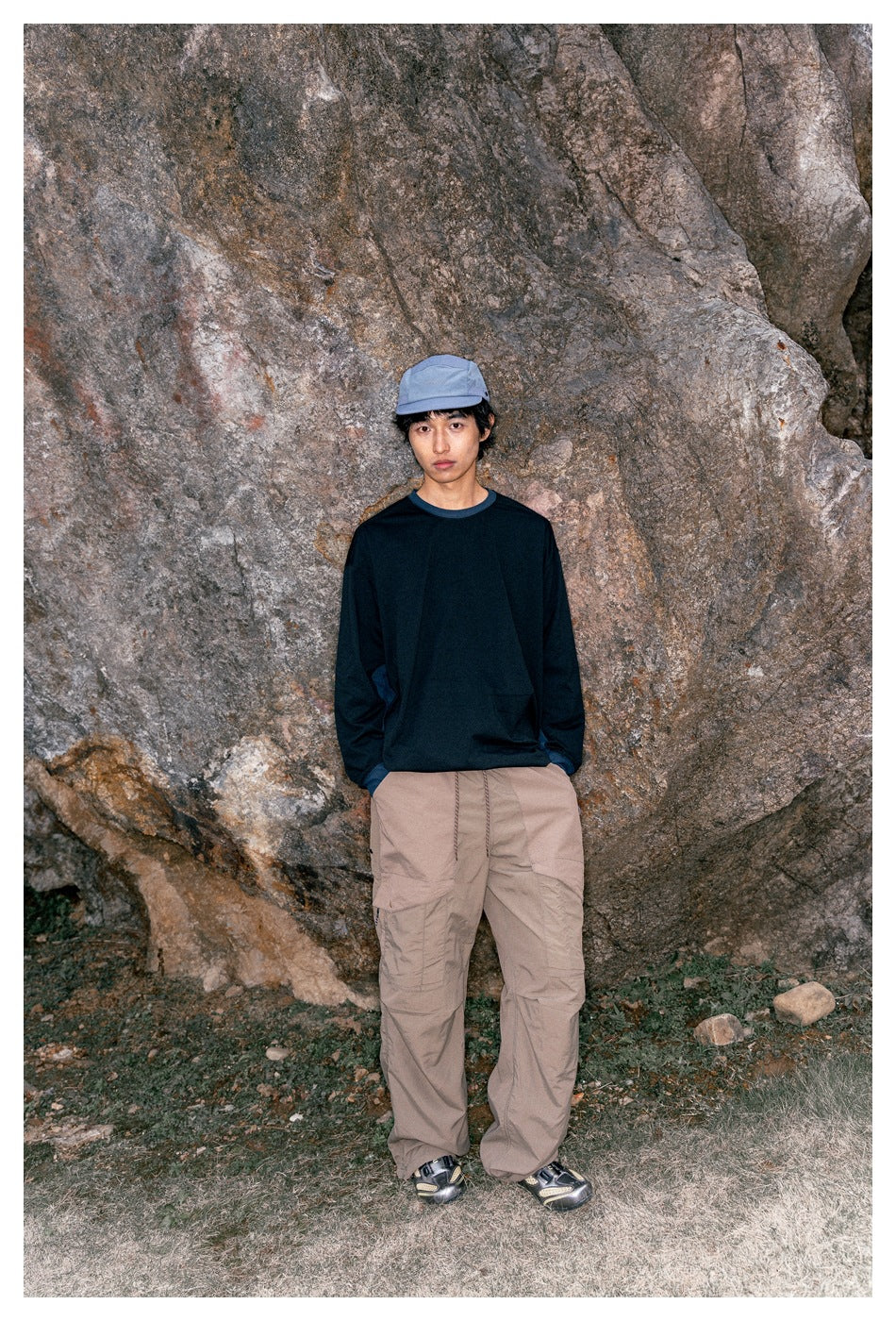 Front view of a model wearing a dark long-sleeve shirt and loose taupe cargo pants outdoors.