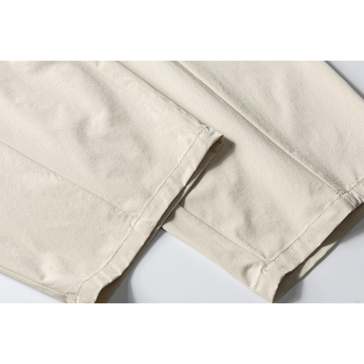 Close-up of cream trouser legs showing the stitched hems and panel seams.