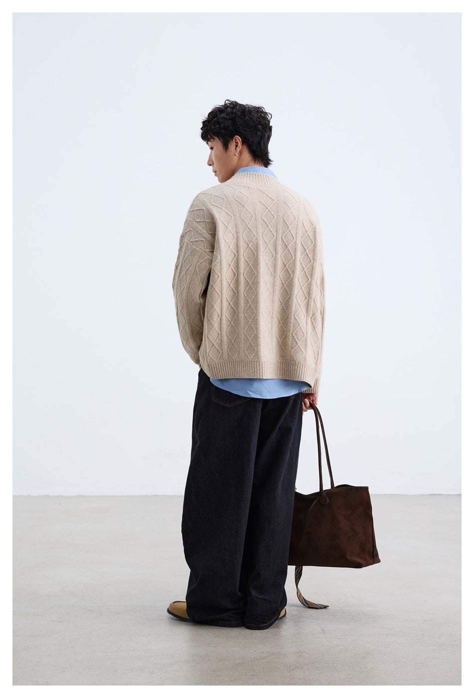 Back view of model wearing a beige diamond-knit cardigan over a blue shirt and dark trousers.