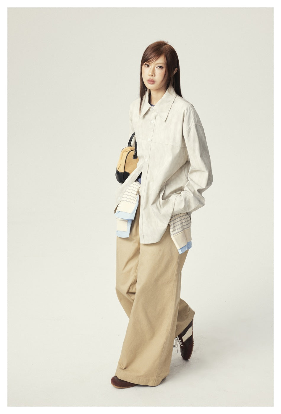 Three-quarter view of a model in an oversized ivory button-up jacket and wide-leg tan trousers.