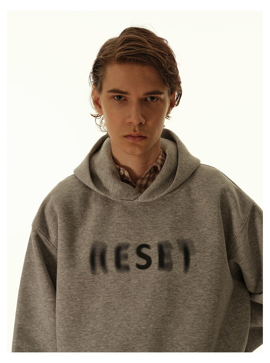 Model wearing a gray hoodie with blurred black lettering over a plaid shirt.