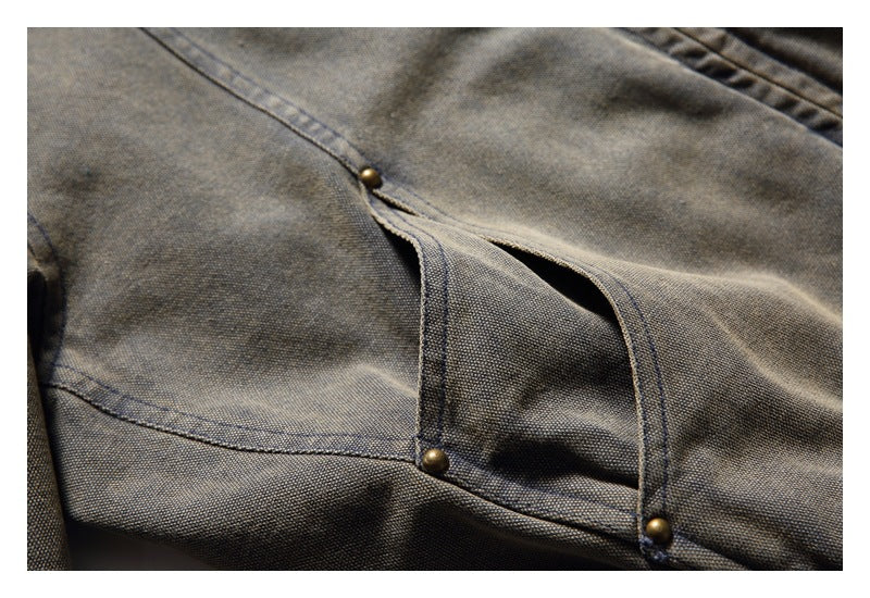 Close-up of a gray-brown jacket pocket opening with stitched edges and small metal rivets.