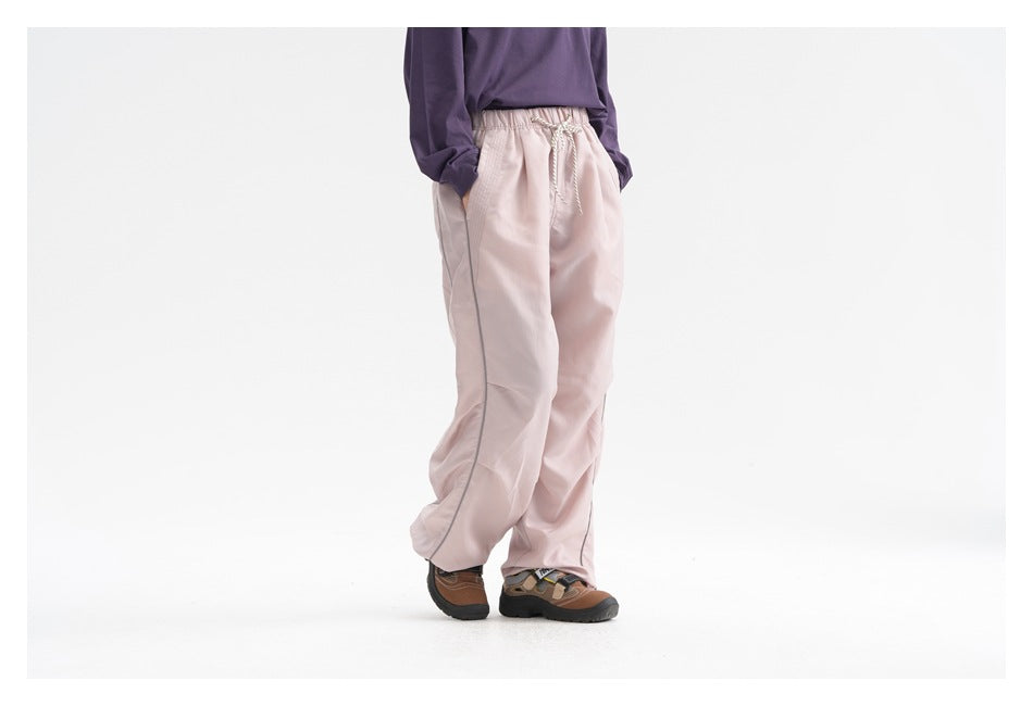 Cropped model wearing pale pink loose drawstring pants with side piping, viewed from the front at an angle.