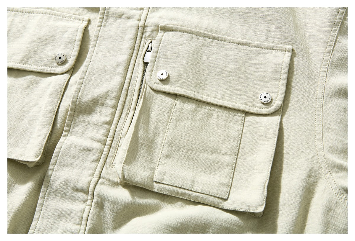 Close-up of a pale beige jacket with layered flap pockets, snap buttons and a vertical zipper.