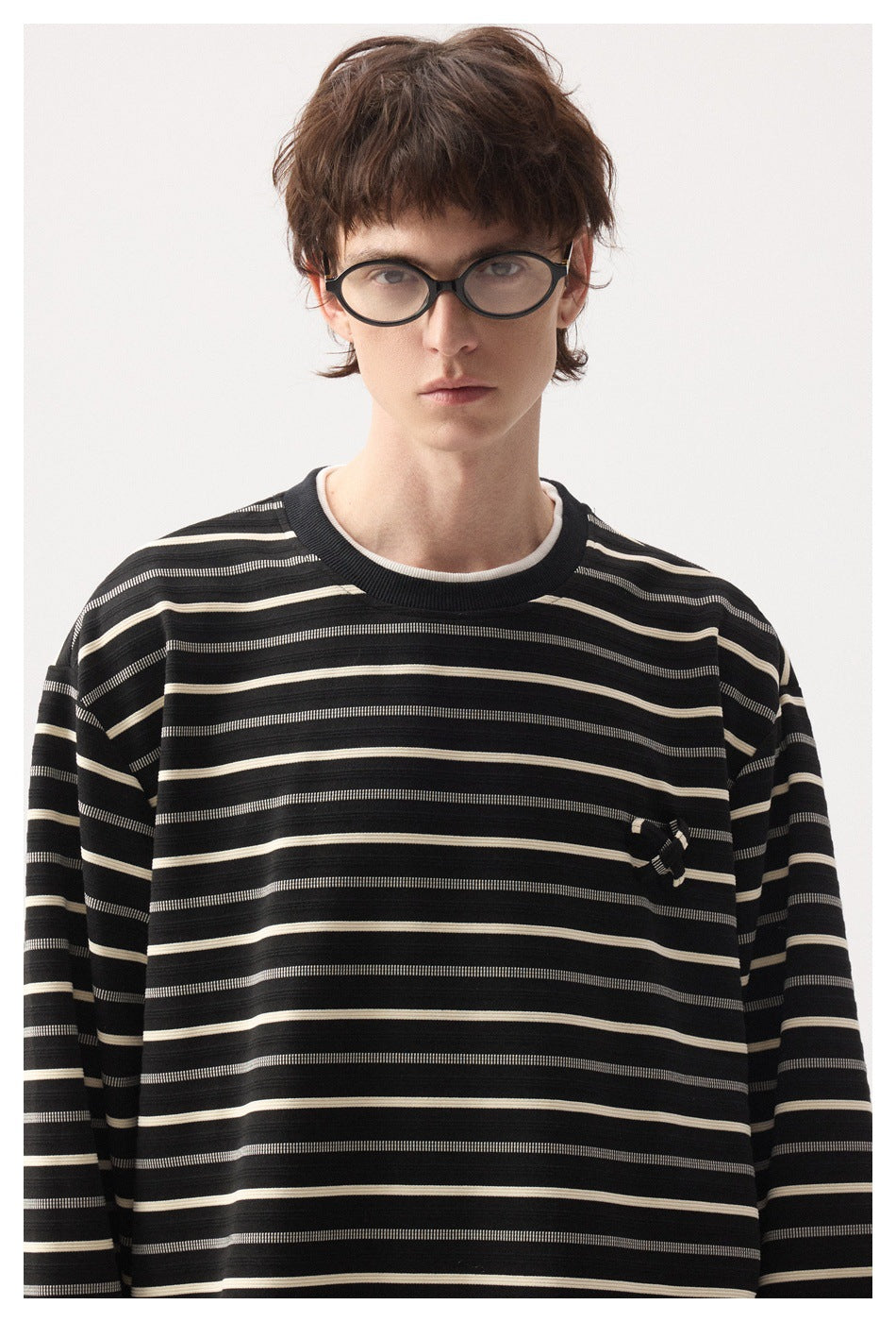 Close view of a model wearing a black striped shirt with a ribbed crew neck and small chest embellishment.
