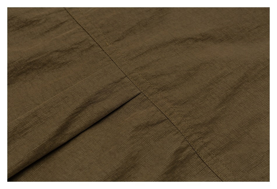 Close-up of olive-brown garment fabric with a diagonal stitched seam and folded panel.