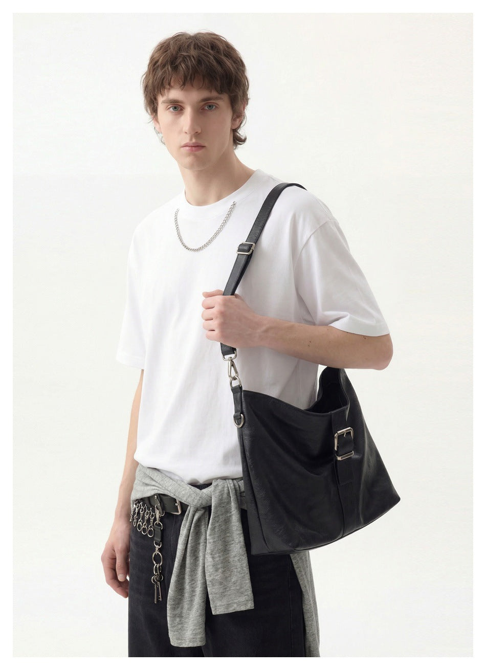 Three-quarter view of a model wearing a plain white crew-neck T-shirt and carrying a black shoulder bag.