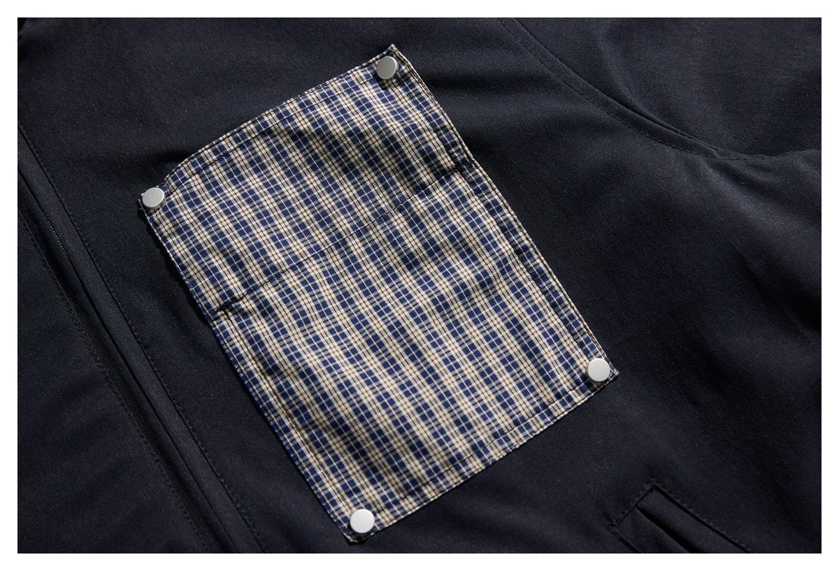 Close-up of a dark garment with a blue-and-cream plaid pocket flap secured by four silver snaps.