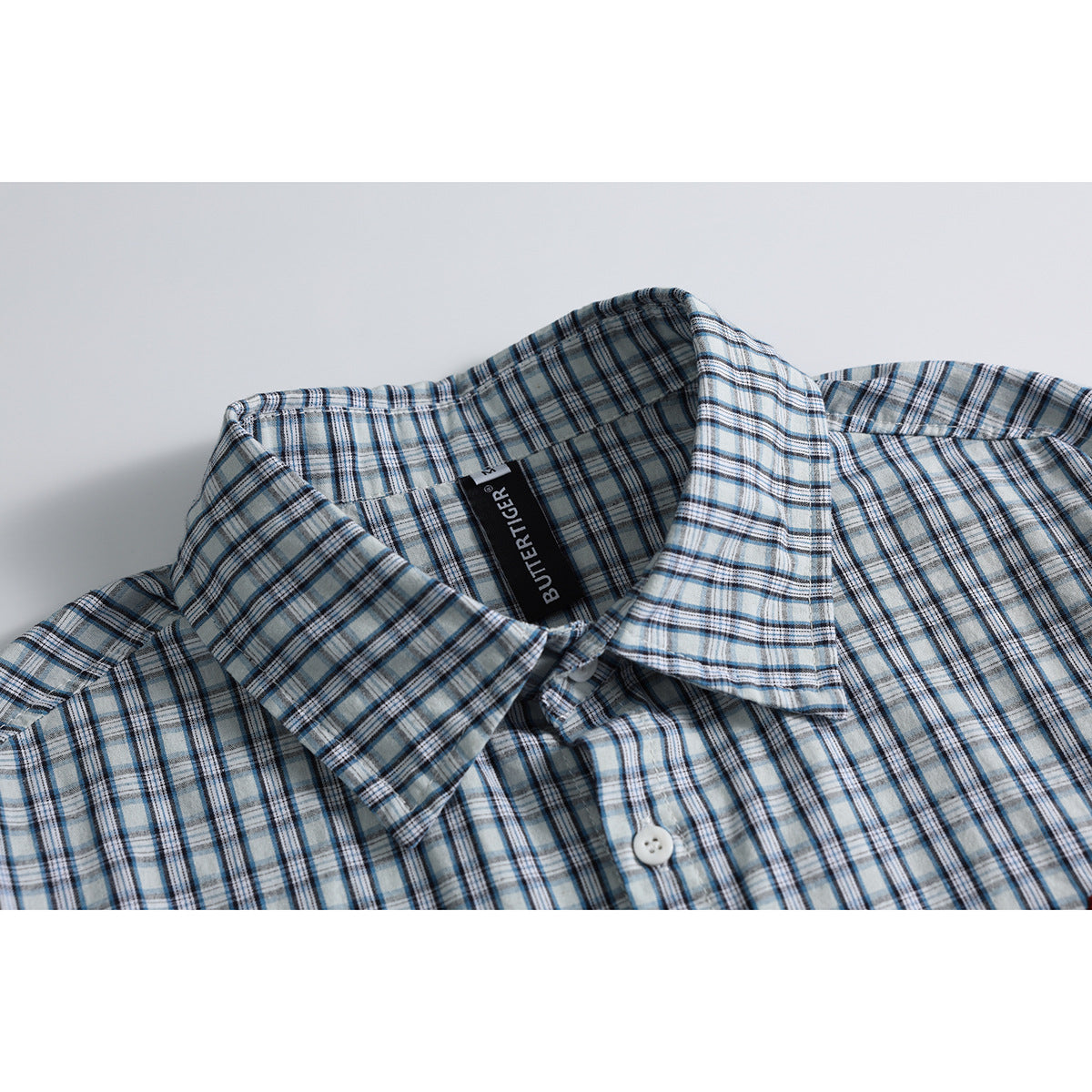 Close-up of a blue, gray, and white plaid shirt collar, placket, and black neck label.