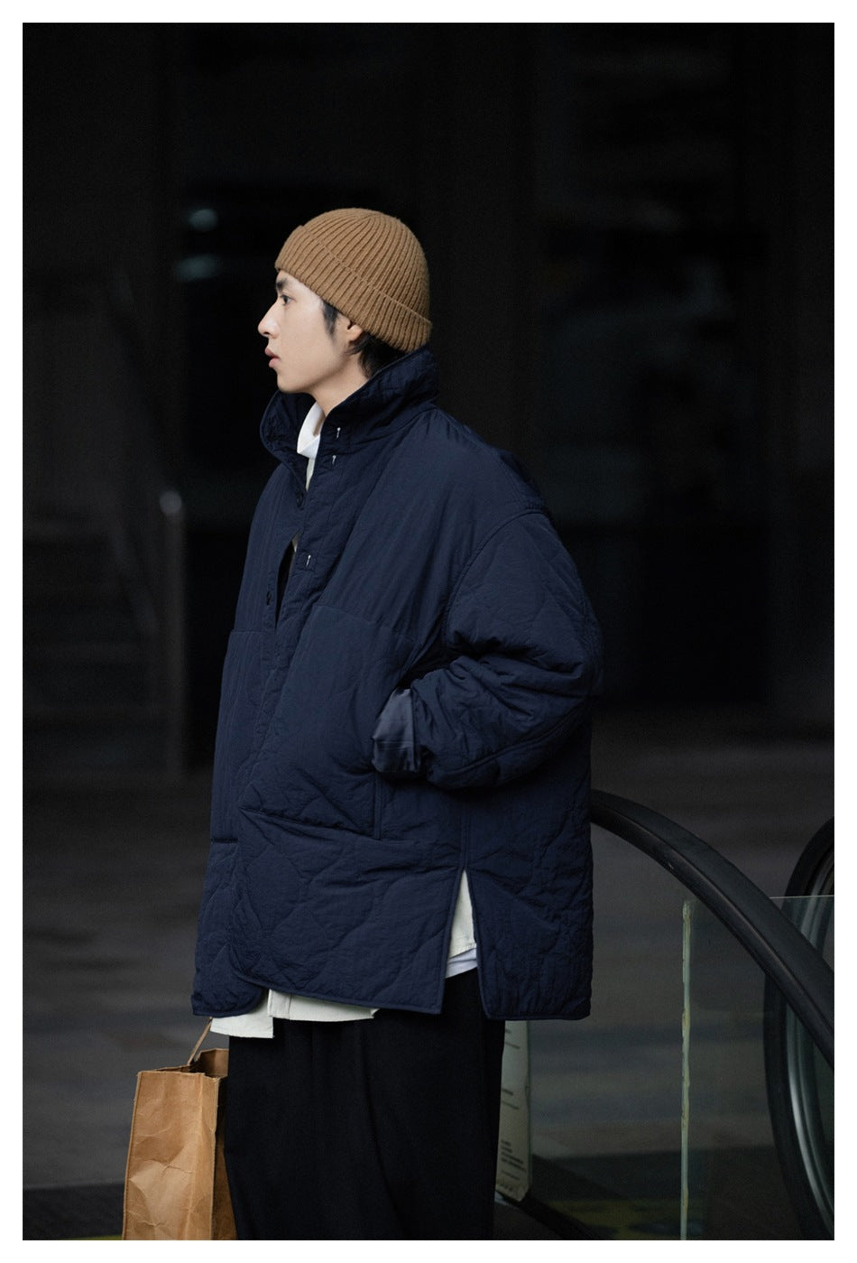 Side view of a model wearing a dark navy quilted coat with a high collar and long, relaxed fit.