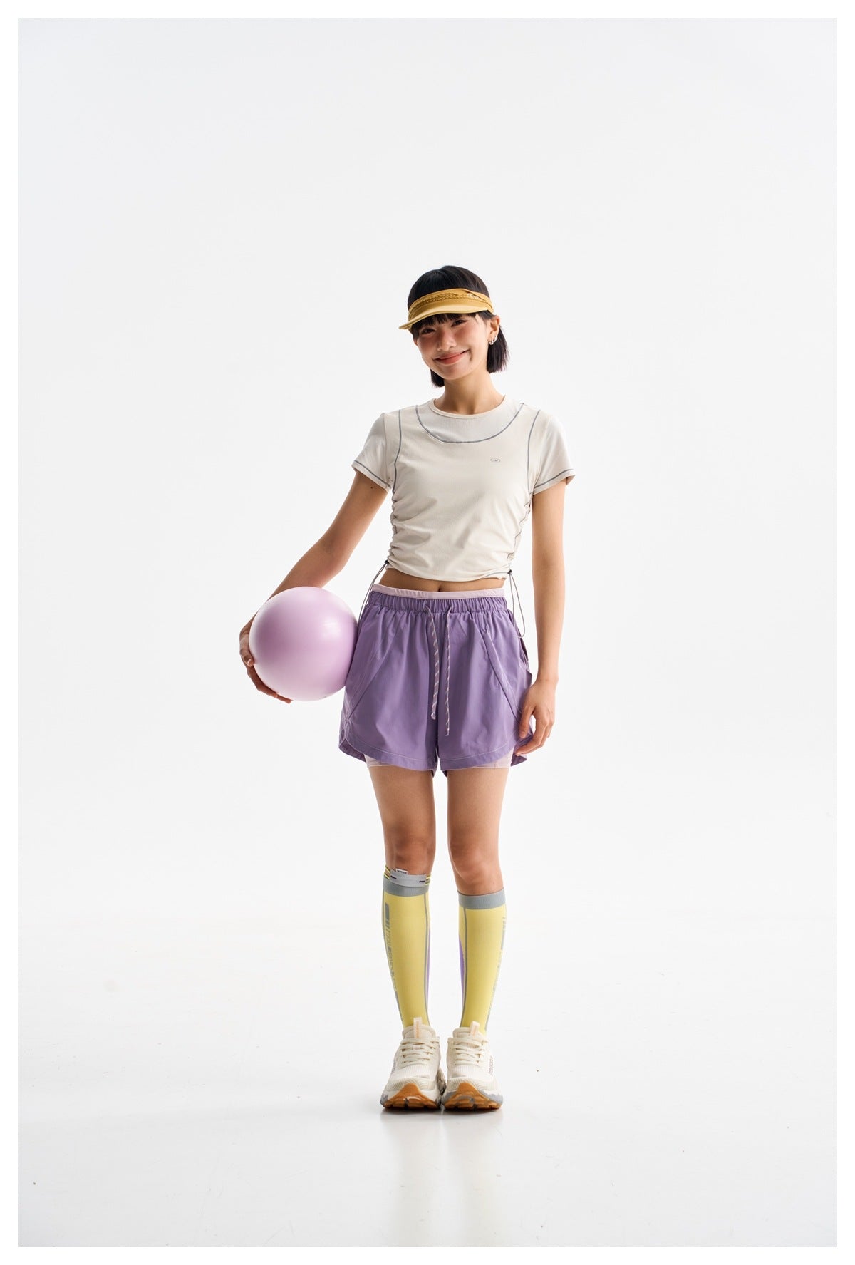 Full-length model wearing a white contrast-seam athletic tee and lavender shorts, holding a lavender ball.