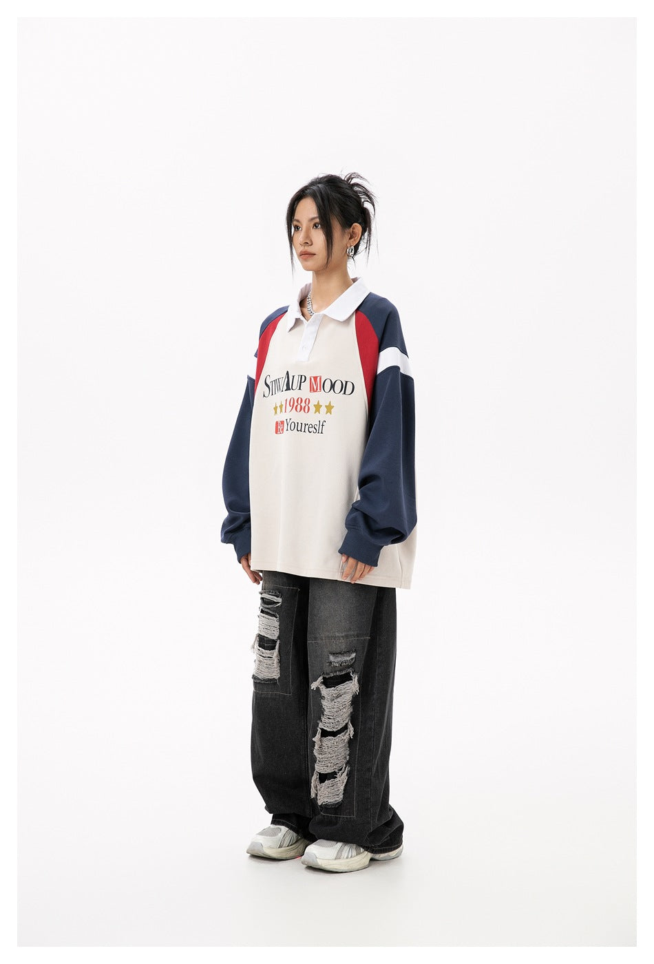 Model wearing the beige and navy oversized polo sweatshirt with ripped black wide-leg jeans, side view
