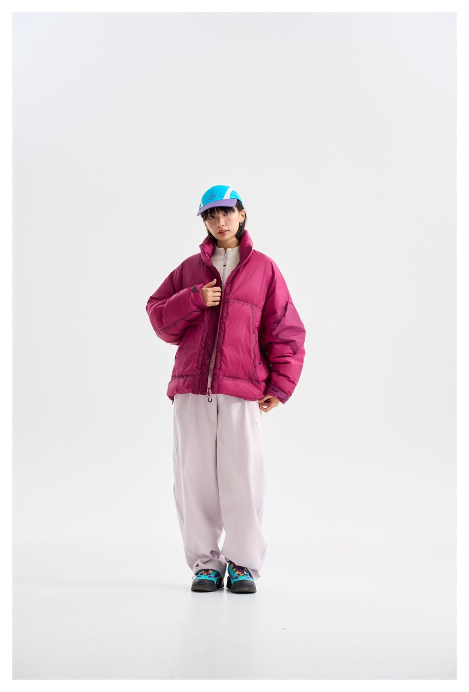 Model shows the magenta puffer jacket worn partly open over a light zip-up top, with pale trousers.
