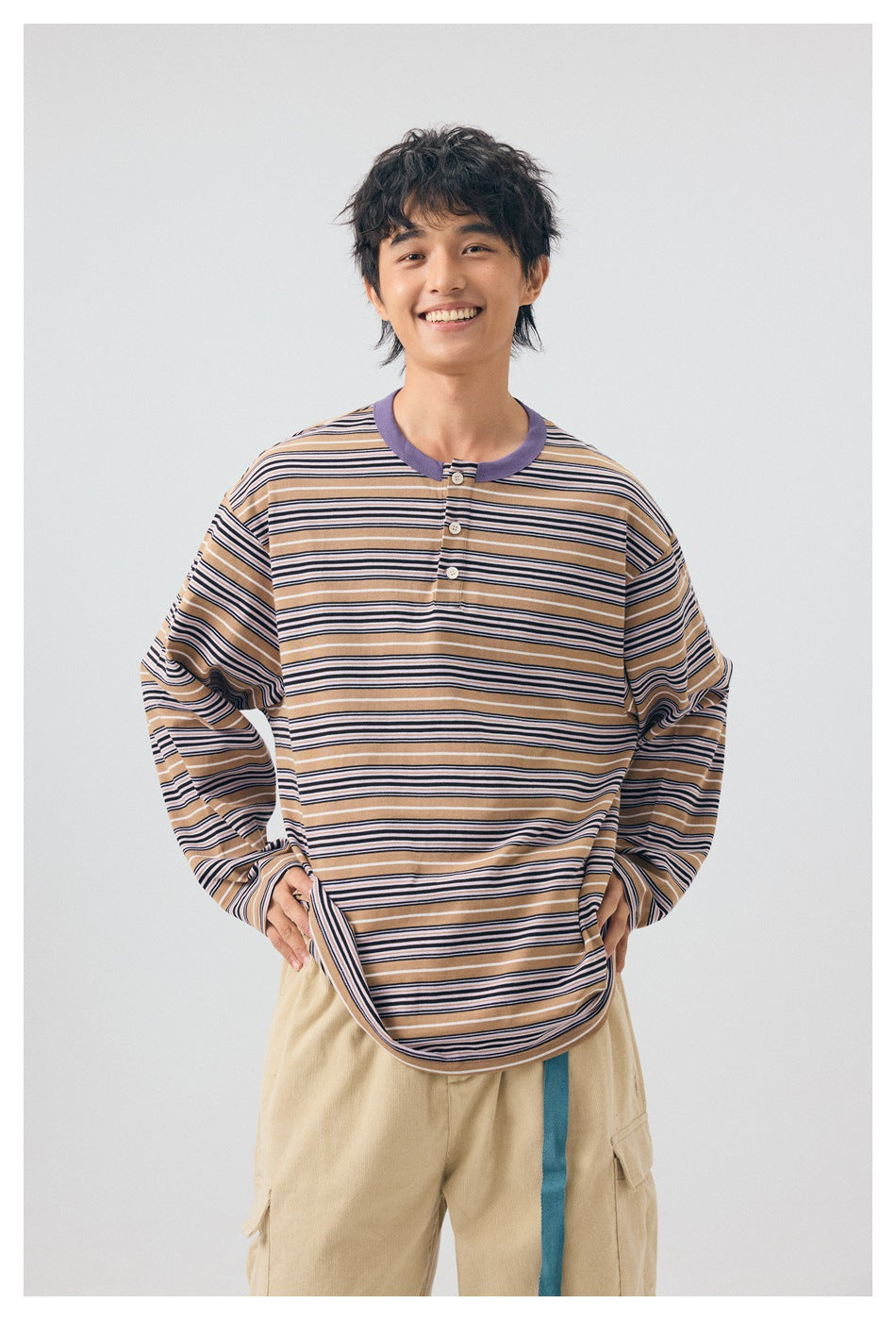 Front view of a model wearing a tan, navy, and white striped long-sleeve henley with a purple collar and three buttons.