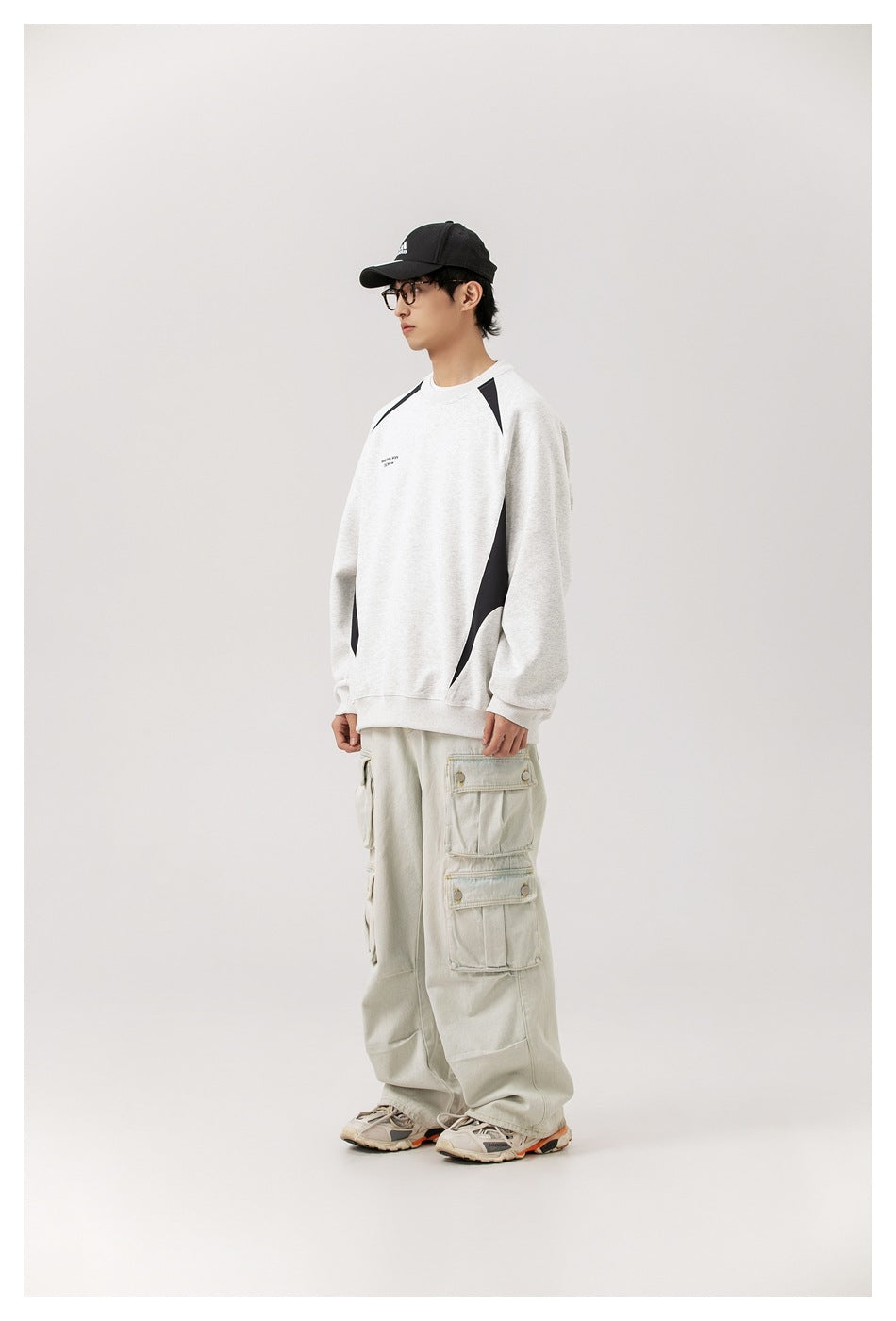 Side view of model in gray crew-neck sweatshirt with black contrast panels, light cargo pants and cap