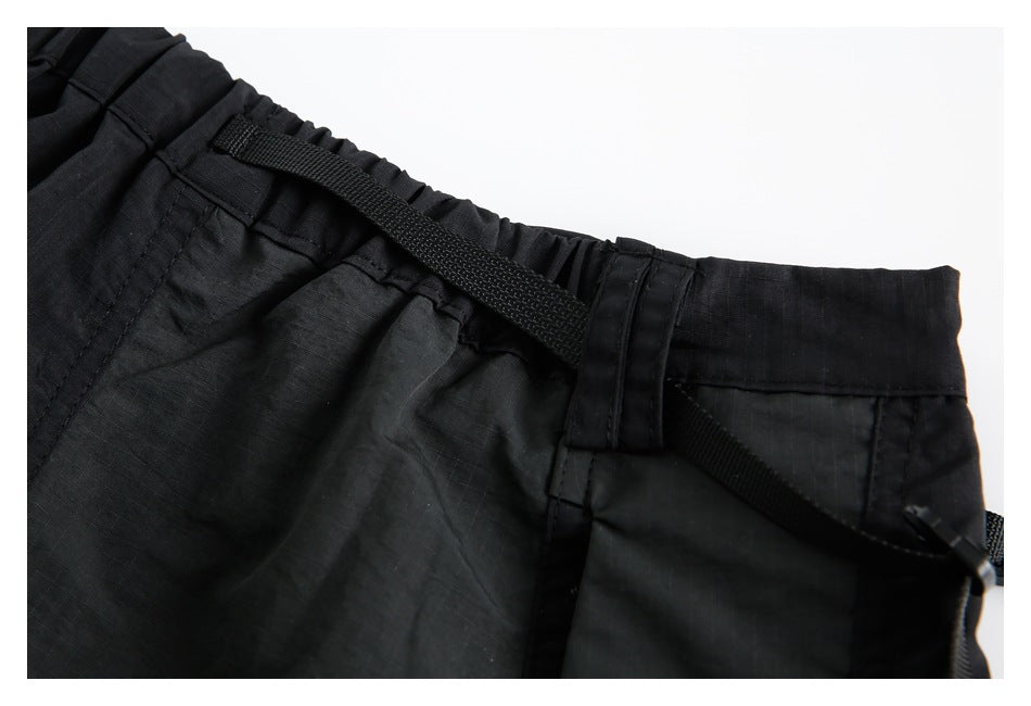 Close-up of black garment waistband with elastic gathering, belt loops, and a webbing strap.