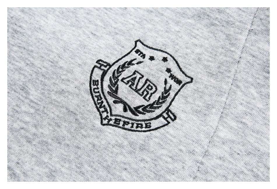 Black embroidered crest on heather-gray fabric, with lettering and a laurel motif.