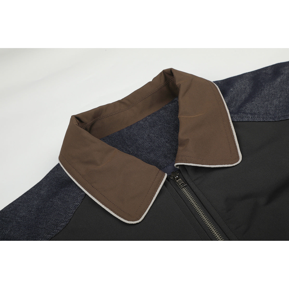 Close-up of a dark jacket with a brown, cream-piped collar, black front panel and zipper, and indigo sleeves.