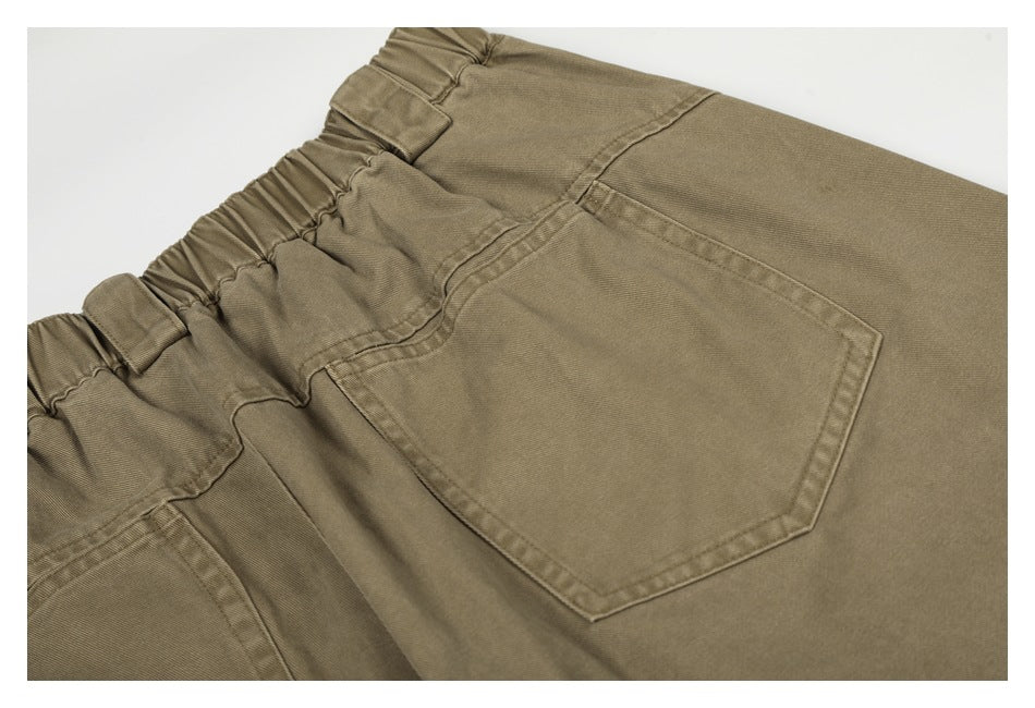 Close-up of olive-khaki trousers showing a gathered elastic waistband and large stitched back pocket.