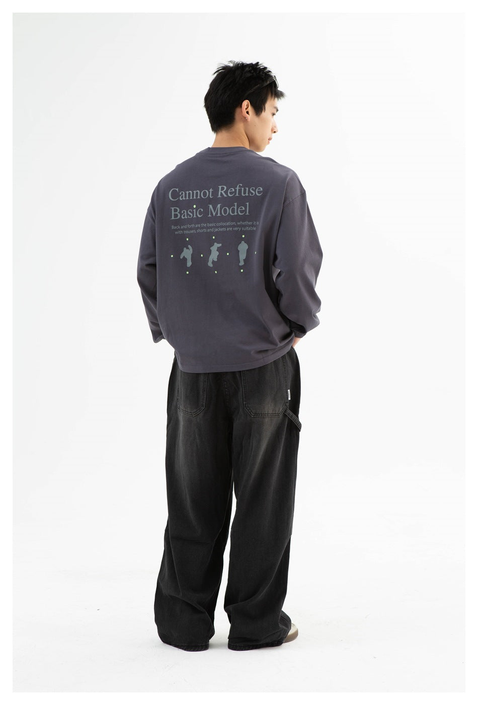 Full-length back view of a model wearing a charcoal-gray graphic long-sleeve top and loose black pants.