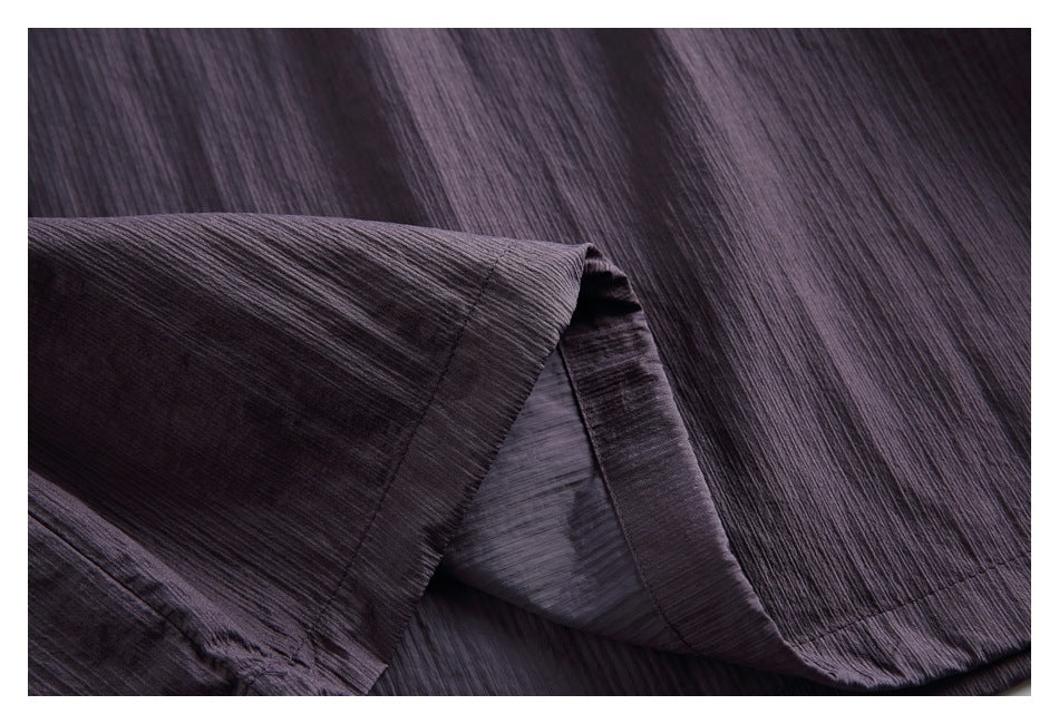 Close-up of a dark charcoal-purple garment with fine ridged texture and a stitched folded hem.